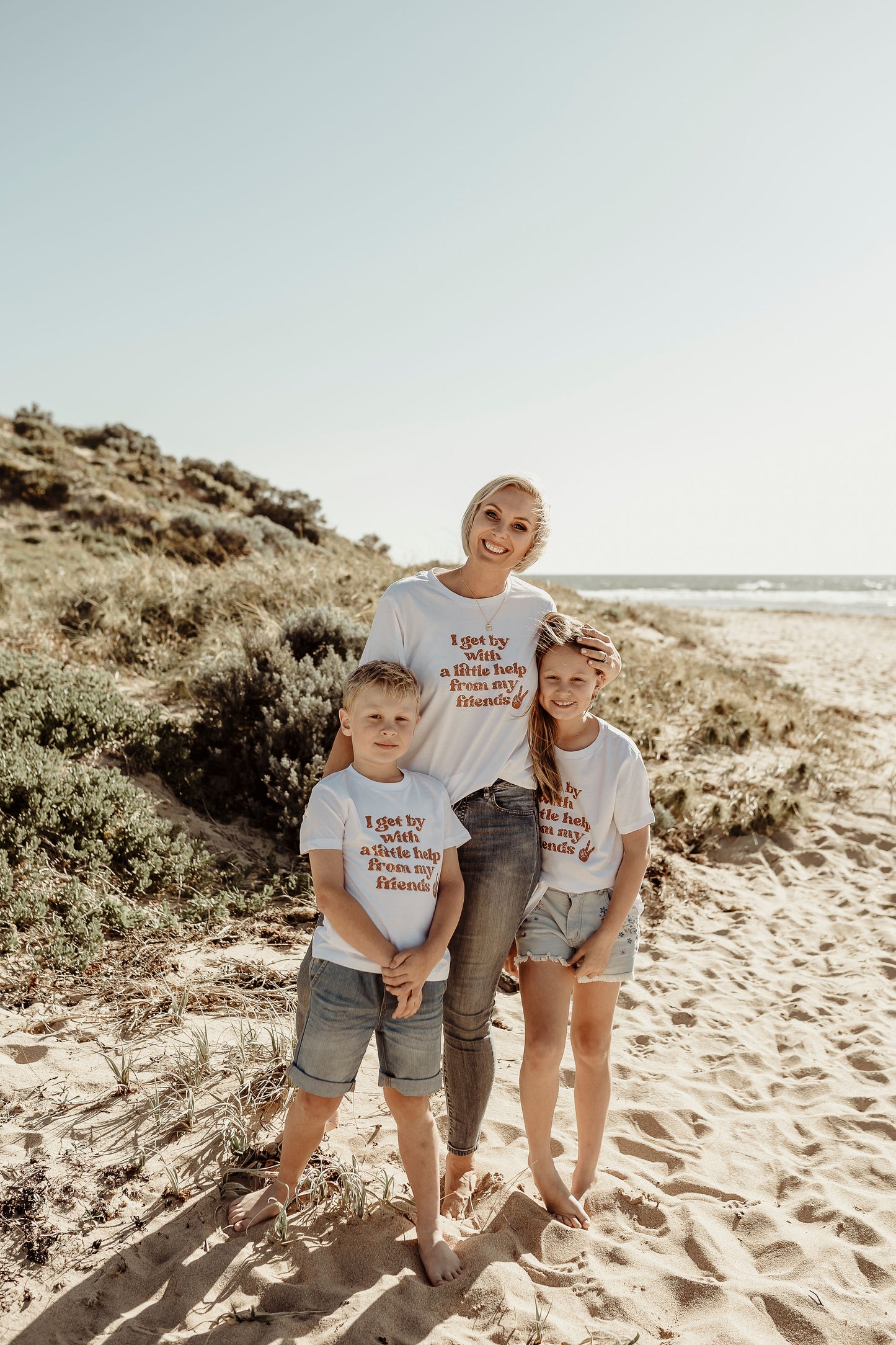 mom with son and daughter posing on the beach wearing I get by with a little help from my friends t shirt in white mental health awareness