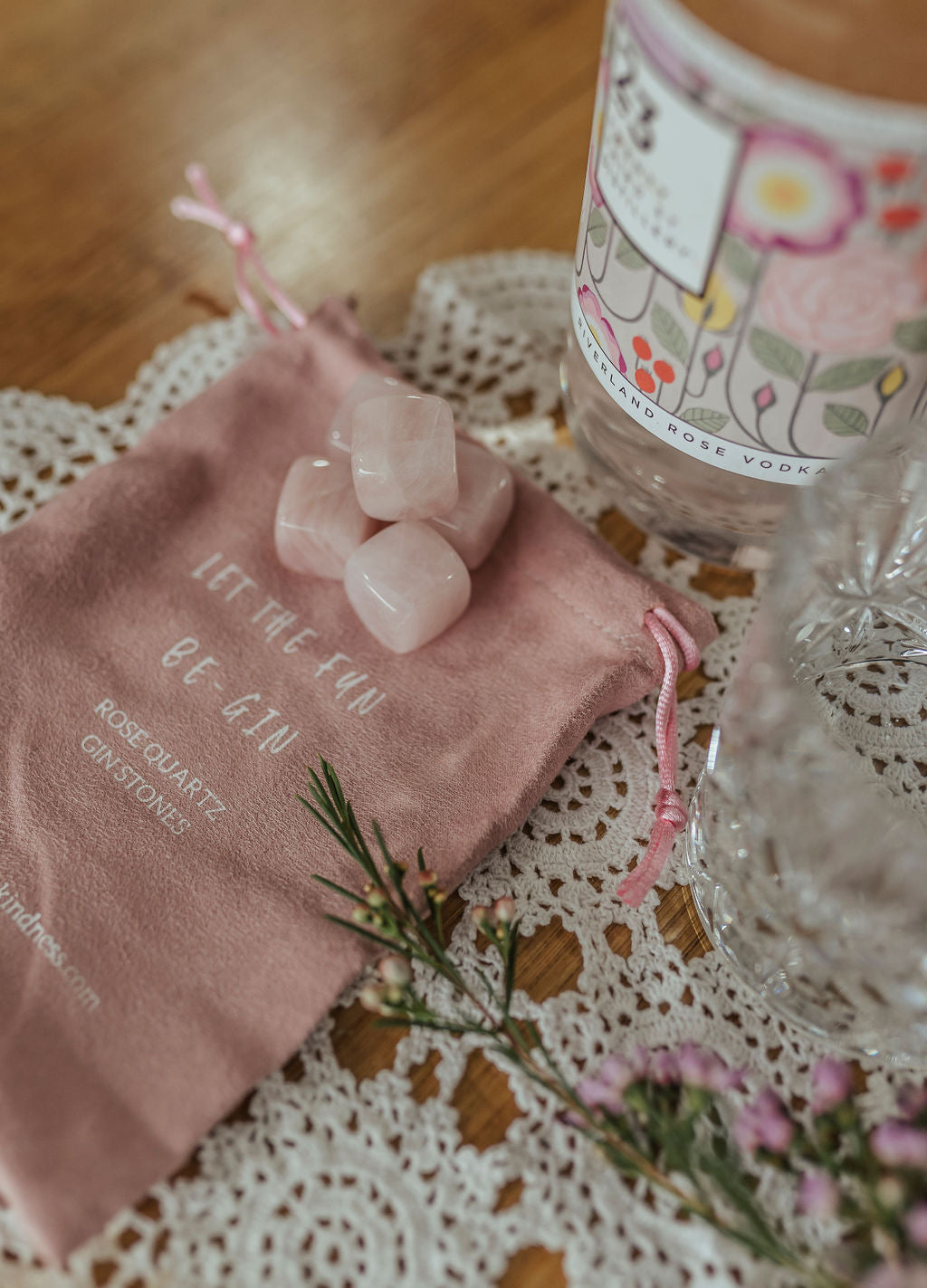 five rose quartz gin stones displayed with pouch, gin bottle and glass in laced mantle