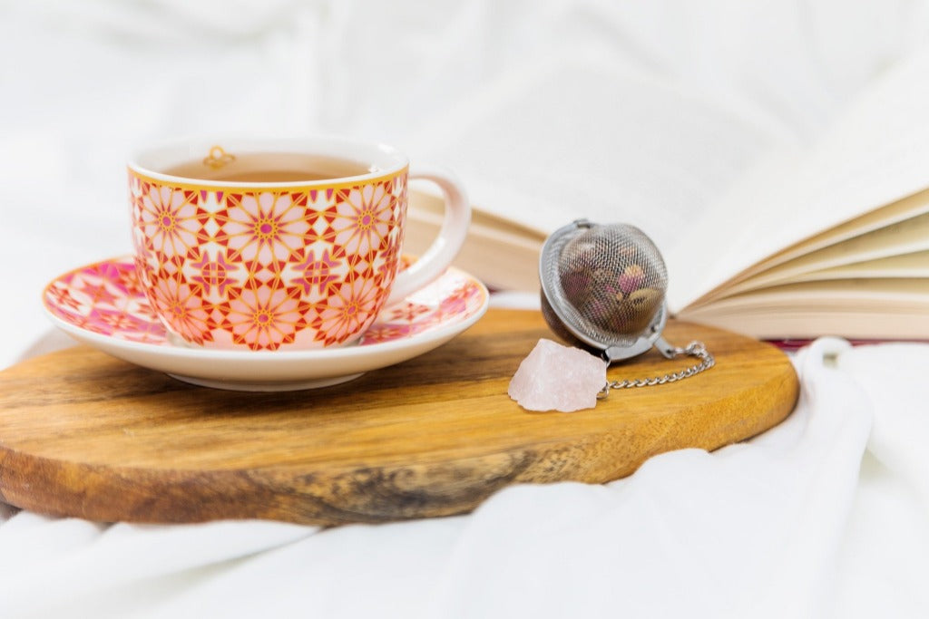 stainless tea strainer with rose quartz for rose tea beside a cup of tea