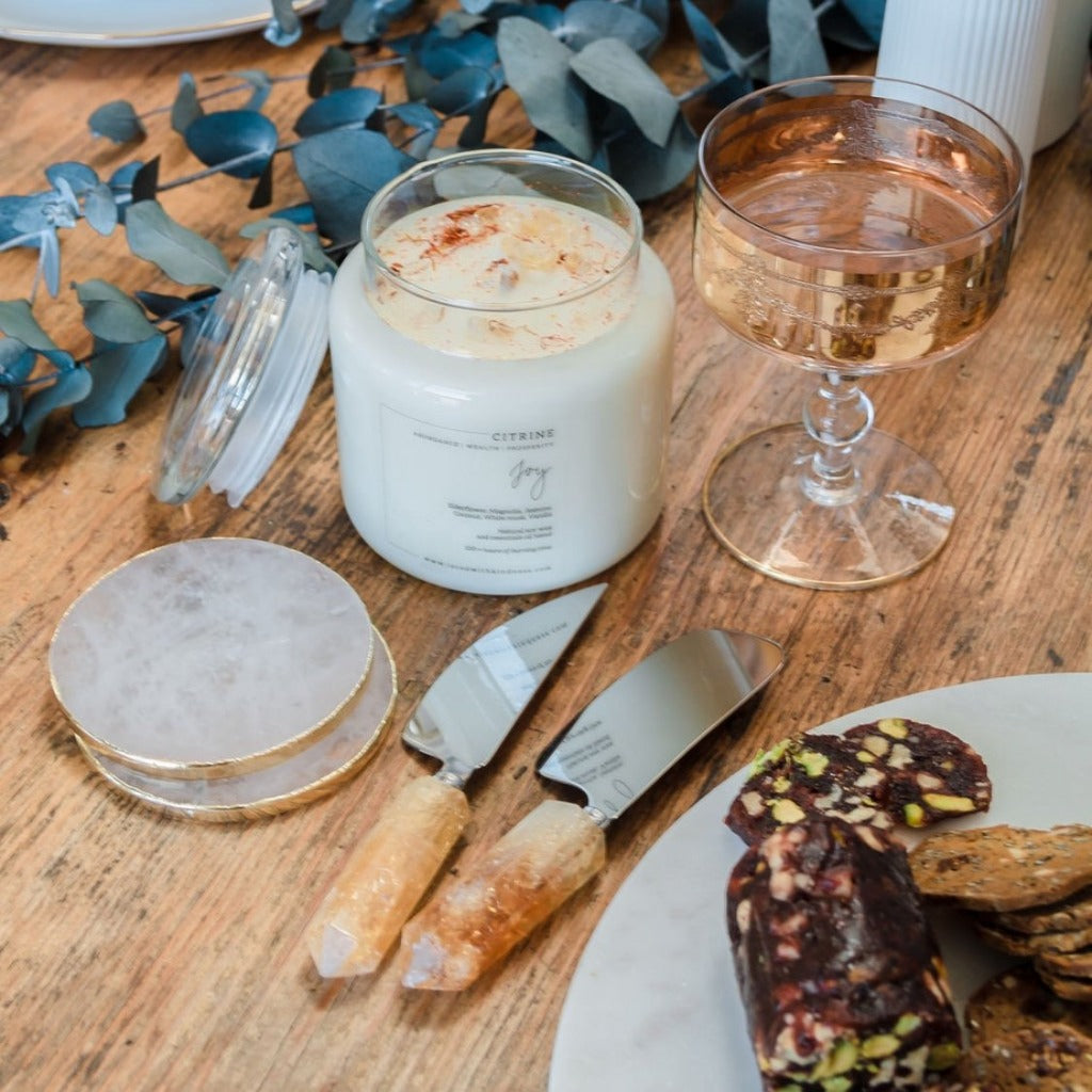Joy Healing candle with citrine , a pair of clear quartz with  luxe gold trim, a pair of citrine crystal cheese knife, in a decorated table