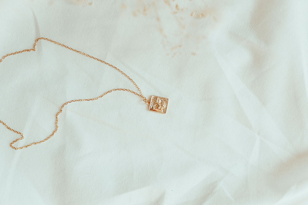 gold heart of lion necklace with square pendant in white fabric background