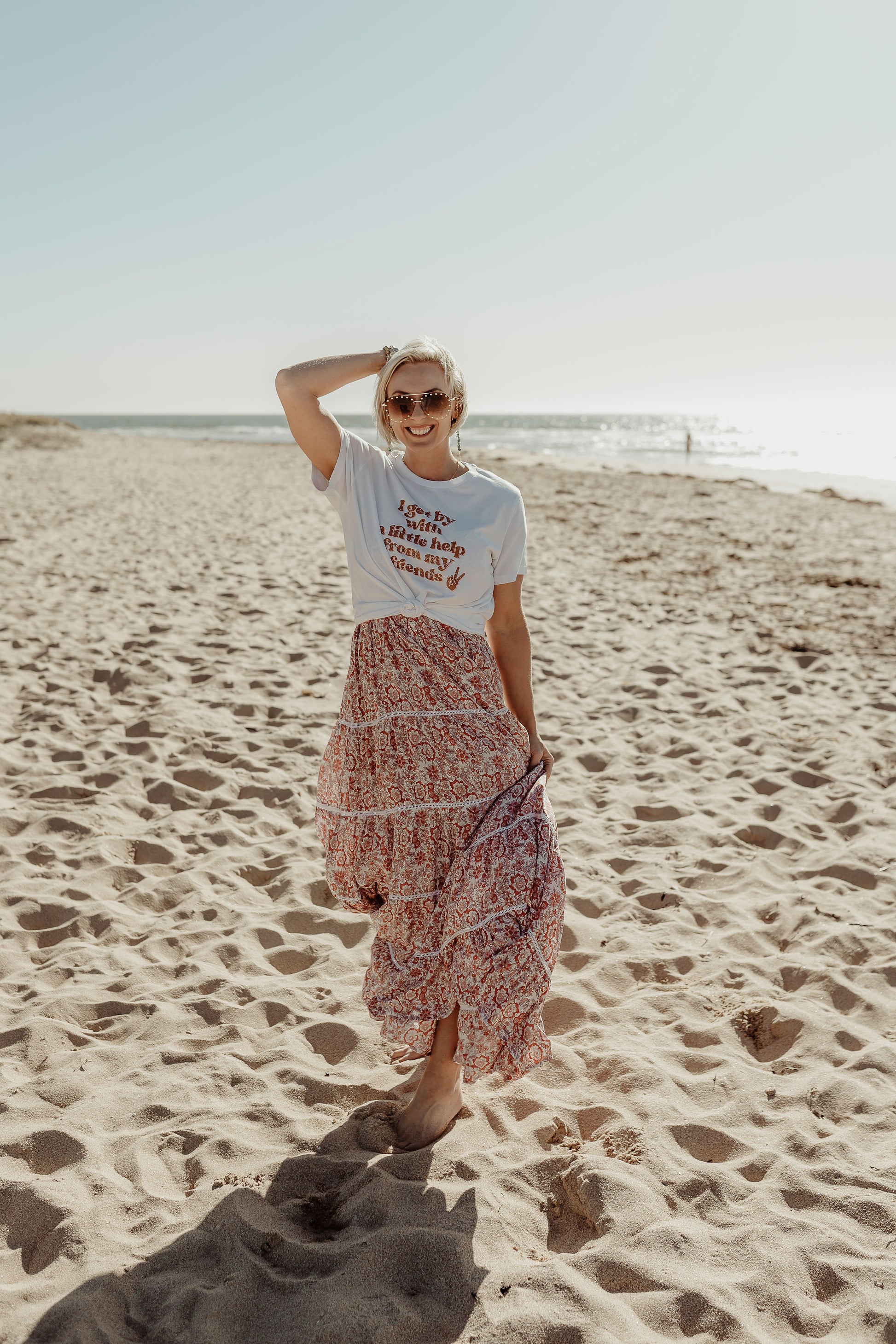 model posing at the beach wearing I get by with a little help with my friends t shirt in white paired with flowy boho skirt mental health awareness